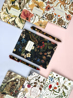 Collection of floral-patterned notebooks and pens on a light pink background