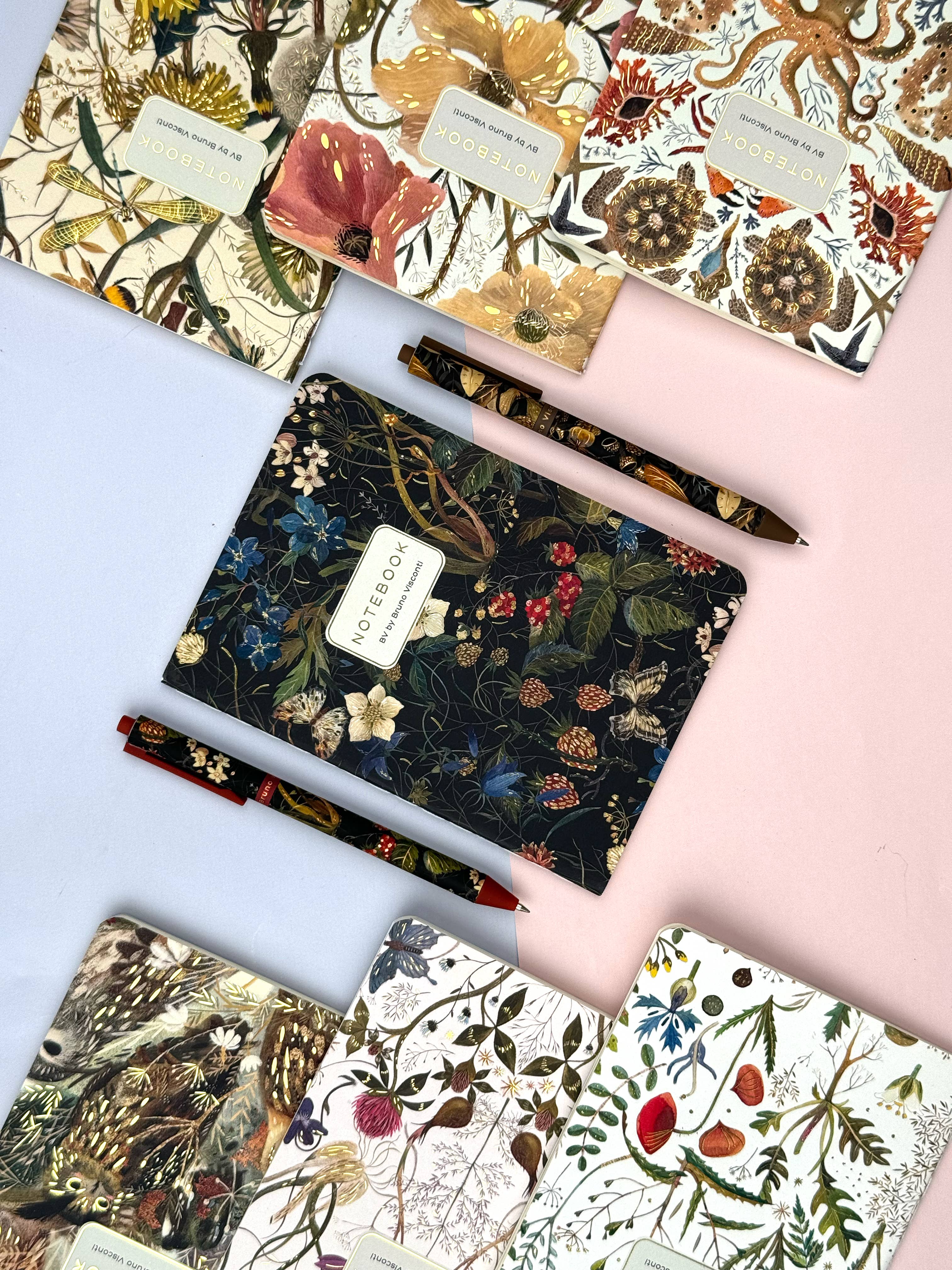 Collection of floral-patterned notebooks and pens on a light pink background