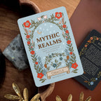 Card with 'Mythic Realms Oracle' design on a wooden surface with decorative elements.