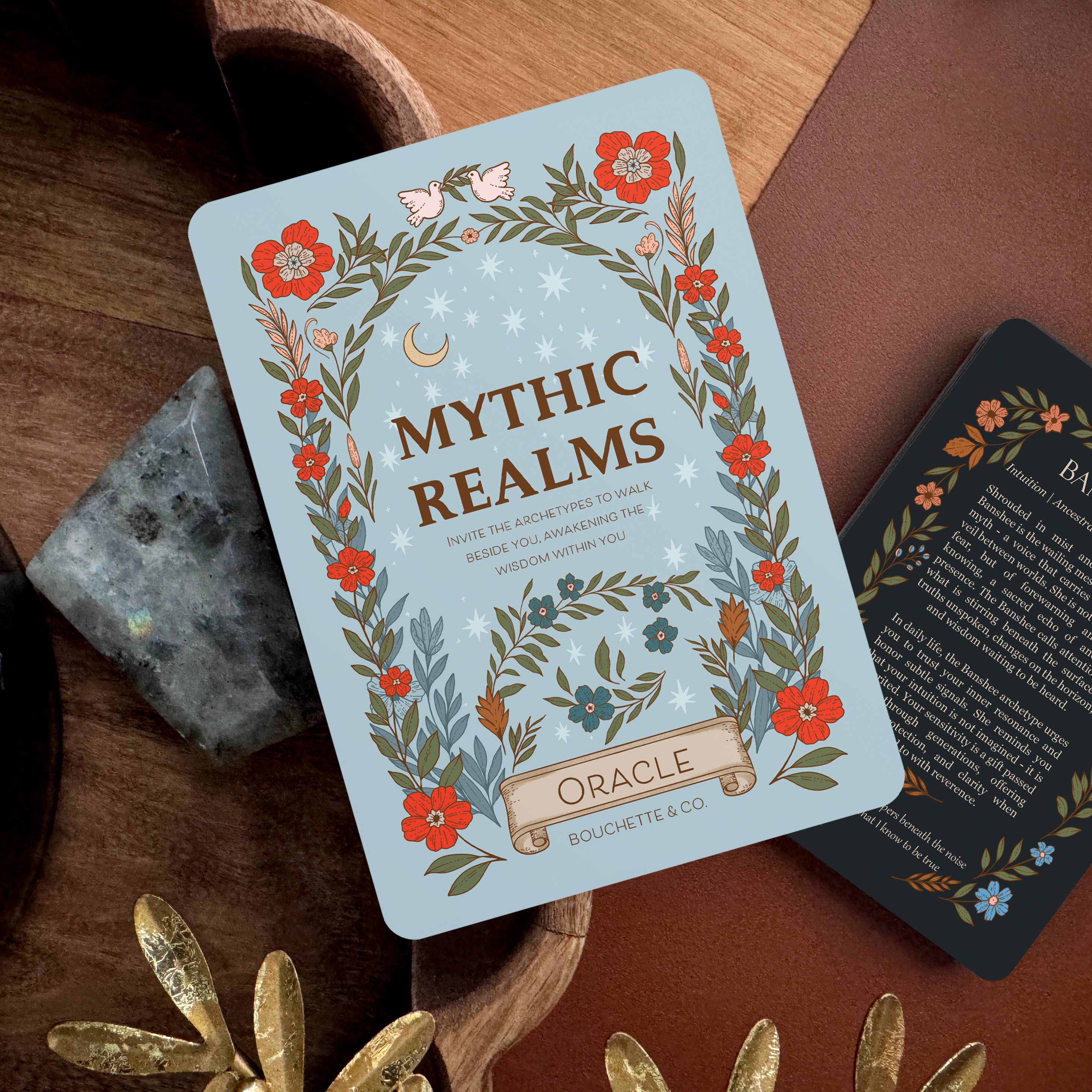 Card with 'Mythic Realms Oracle' design on a wooden surface with decorative elements.