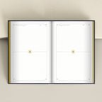 An open planner or notebook with two blank white interior spreads, each featuring a gold star motif near the center and subtle decorative corner details, photographed from above against a light beige background.