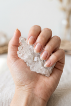 Hand holding a crystal cluster against a neutral background
