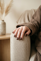 Person wearing a brown coat with a hand resting on a beige armchair.