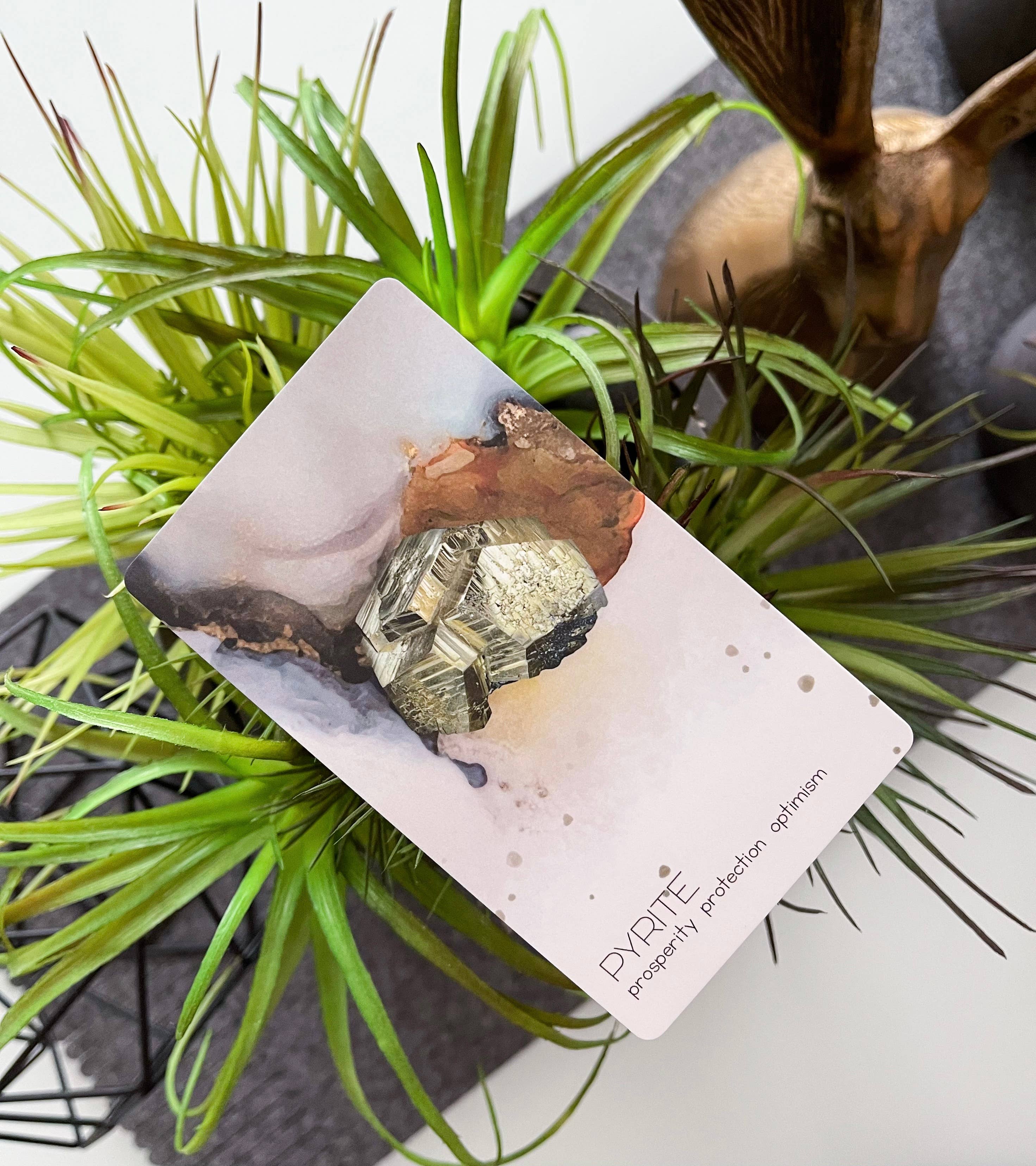 Card with pyrite crystals on a plant and decorative deer head background