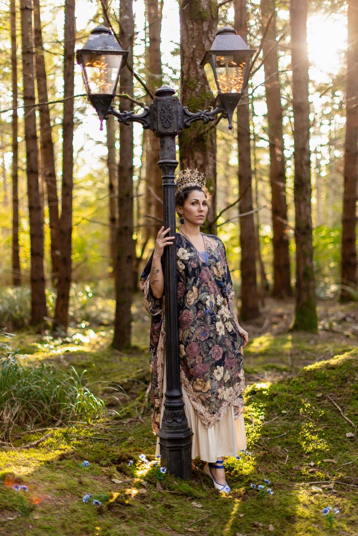Woman in a floral dress standing next to a vintage lamp post in a forest