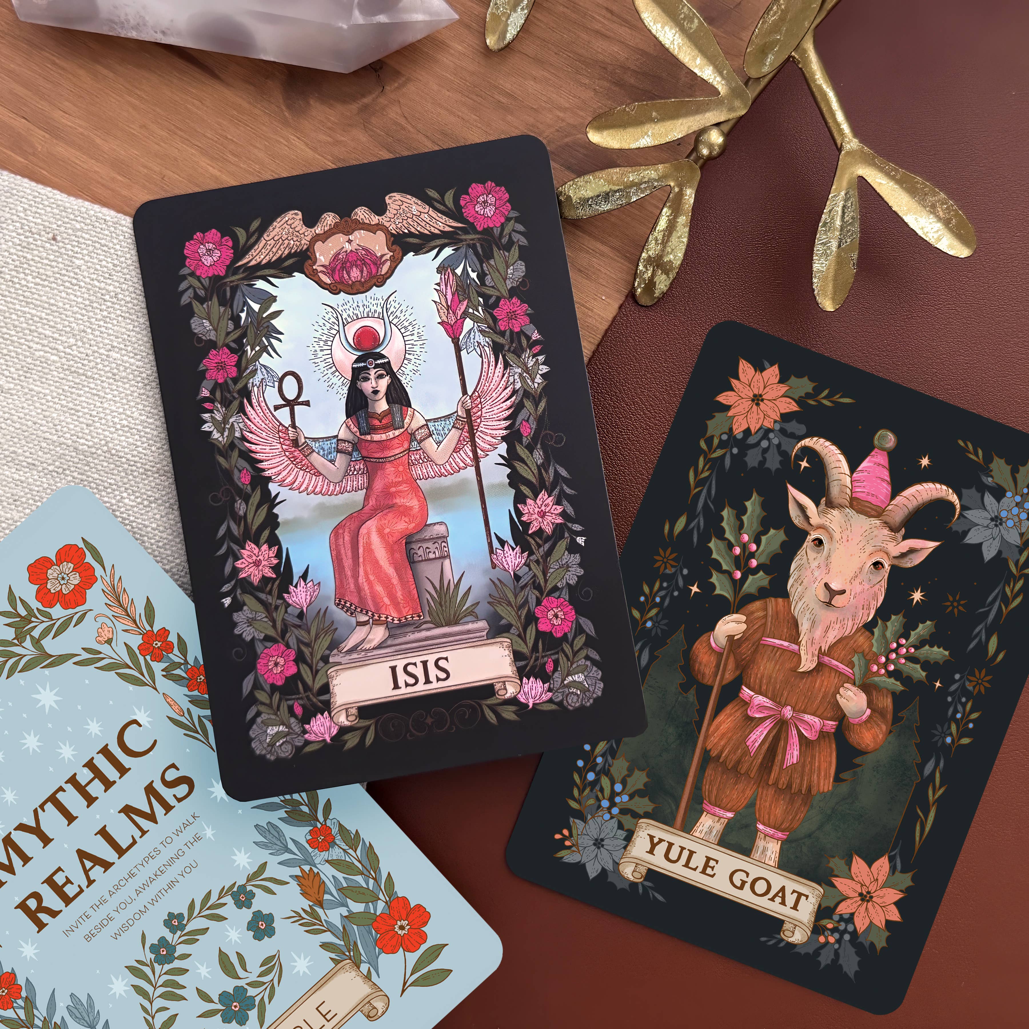 Two tarot cards featuring 'Isis' and 'Yule Goat' on a wooden surface with decorative elements.