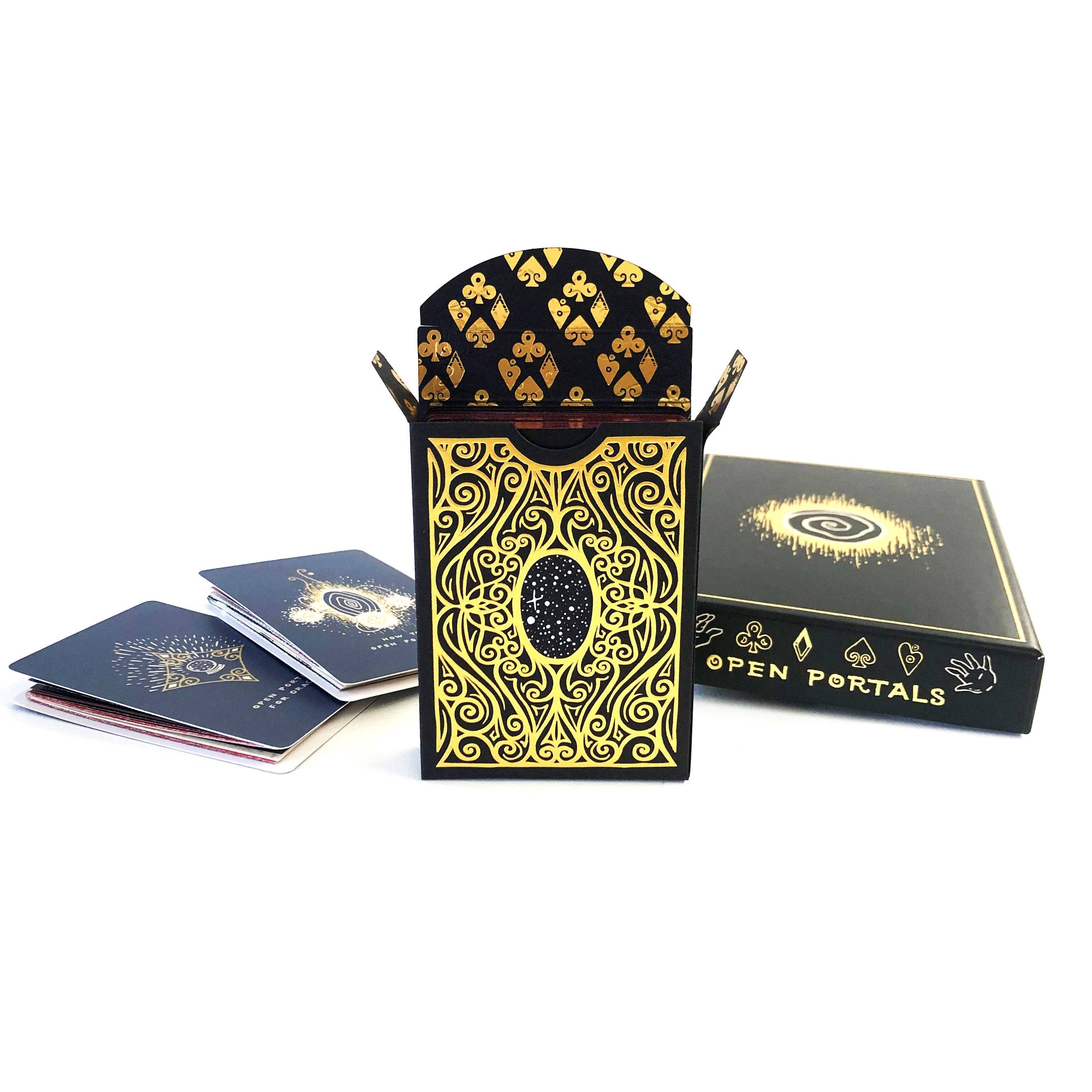 A black and gold deck of playing cards with ornate filigree patterns, shown with an open card holder, a closed box labeled 'OPEN PORTALS,' and a few cards on a white background.