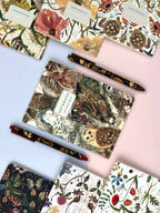 Collection of notebooks with nature-themed designs and matching pens on a light blue background.