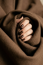 Close-up of a hand with dark nail polish holding brown fabric