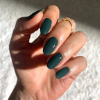 Hand with dark green nails and a gold ring on a textured white background