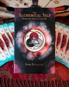 The Alchemical Self Altar and Oracle Card Set box by Anna Bousquet, displayed upright with cards fanned out on both sides on a red patterned textile.