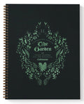 A spiral-bound yearly planner titled 'The Garden' from 'A Vital Plant Parade', featuring a botanical wreath design in mint green on a matte black cover.