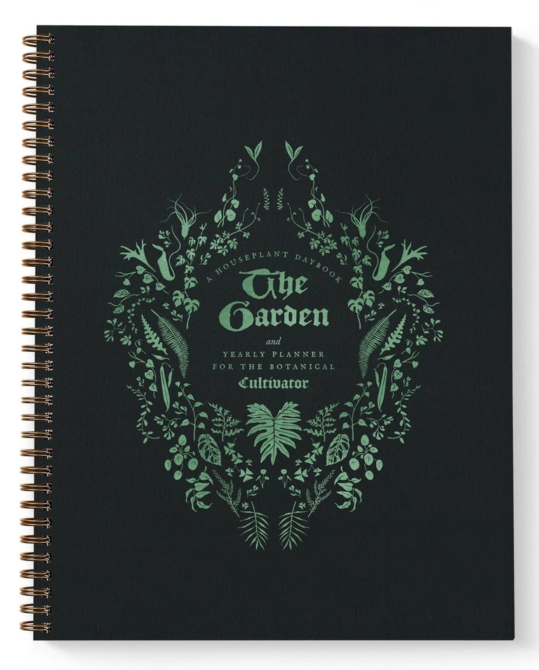 A spiral-bound yearly planner titled 'The Garden' from 'A Vital Plant Parade', featuring a botanical wreath design in mint green on a matte black cover.