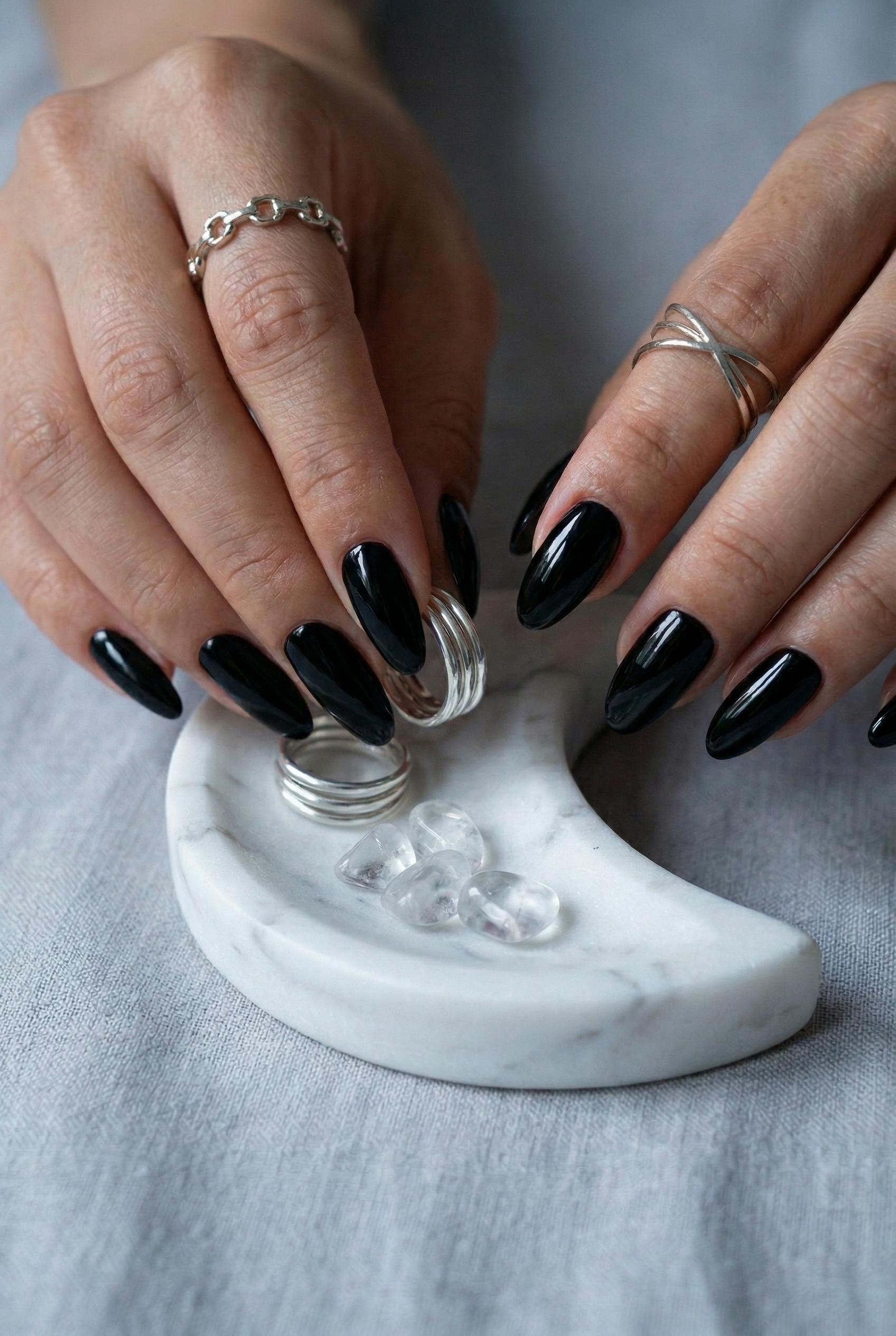 Close-up of hands with black nail polish holding a marble ring holder with rings on a gray background