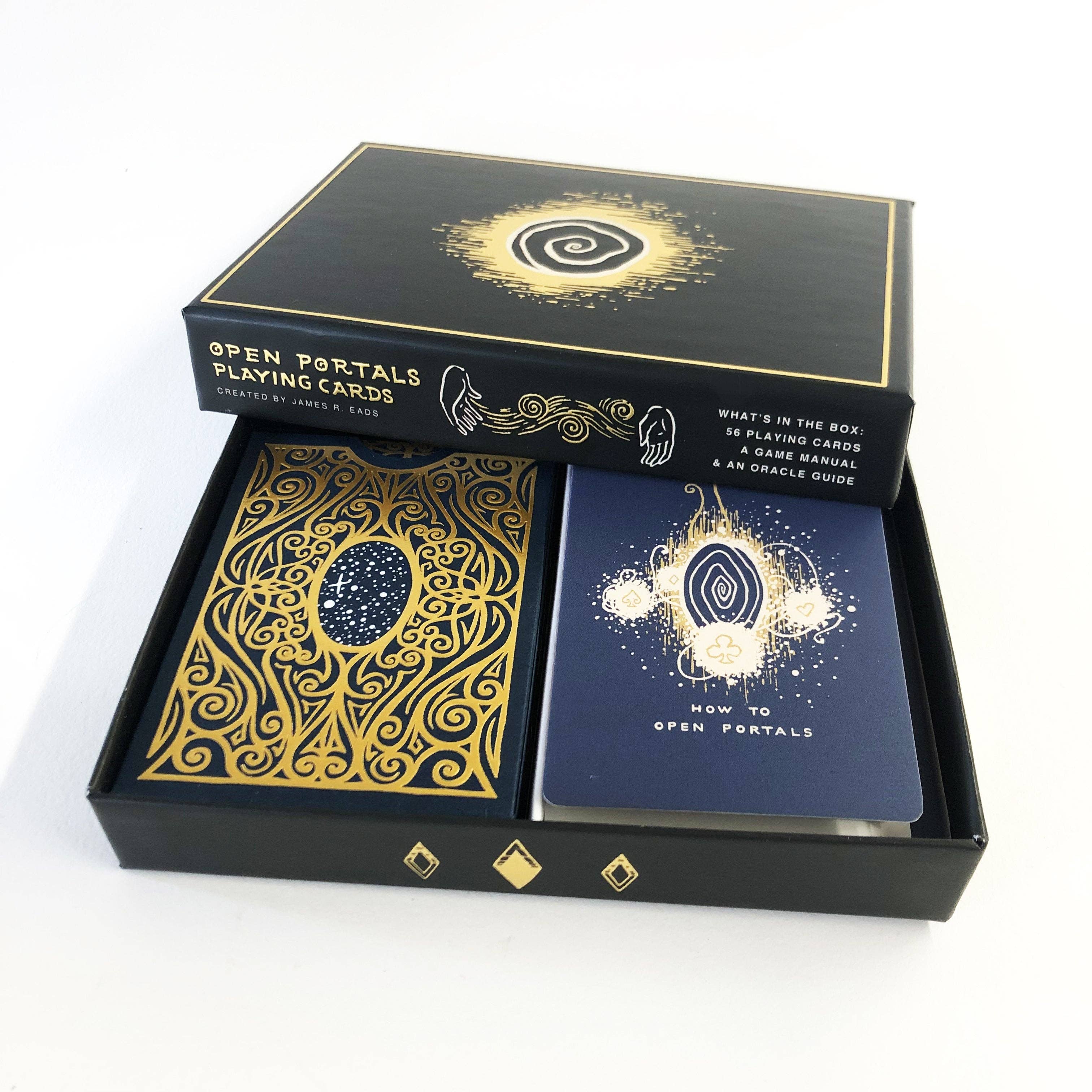 Open Portals Playing Cards deck in its black presentation box, showing the outer box lid, a card back with ornate gold filigree, and a blue instruction card with gold artwork.
