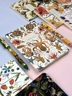 Collection of notebooks with floral and nature-themed designs on a pink surface.