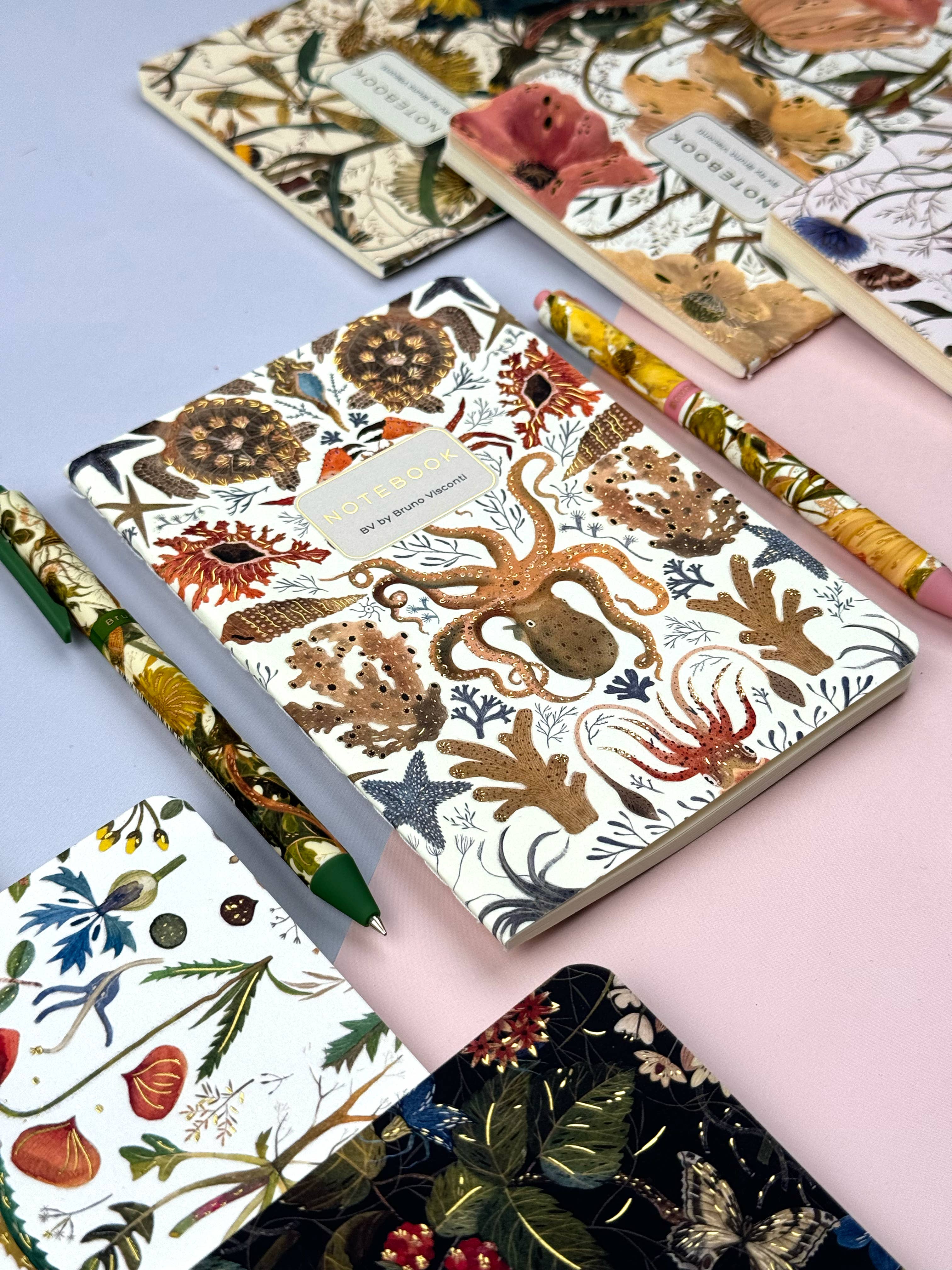 Collection of notebooks with floral and nature-themed designs on a pink surface.