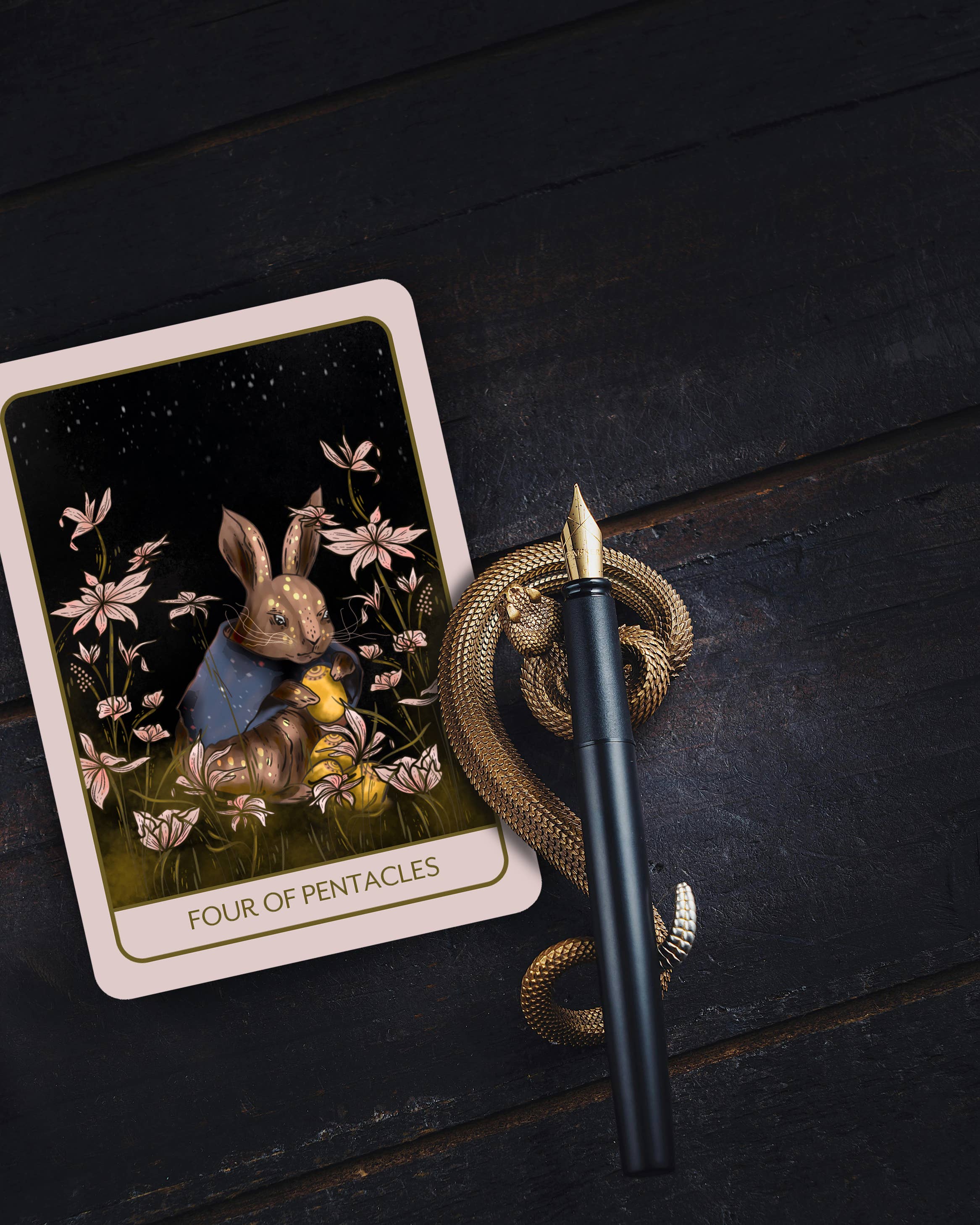 A tarot card titled 'FOUR OF PENTACLES' lies on a dark wooden surface next to a coiled gold pen with a black grip.