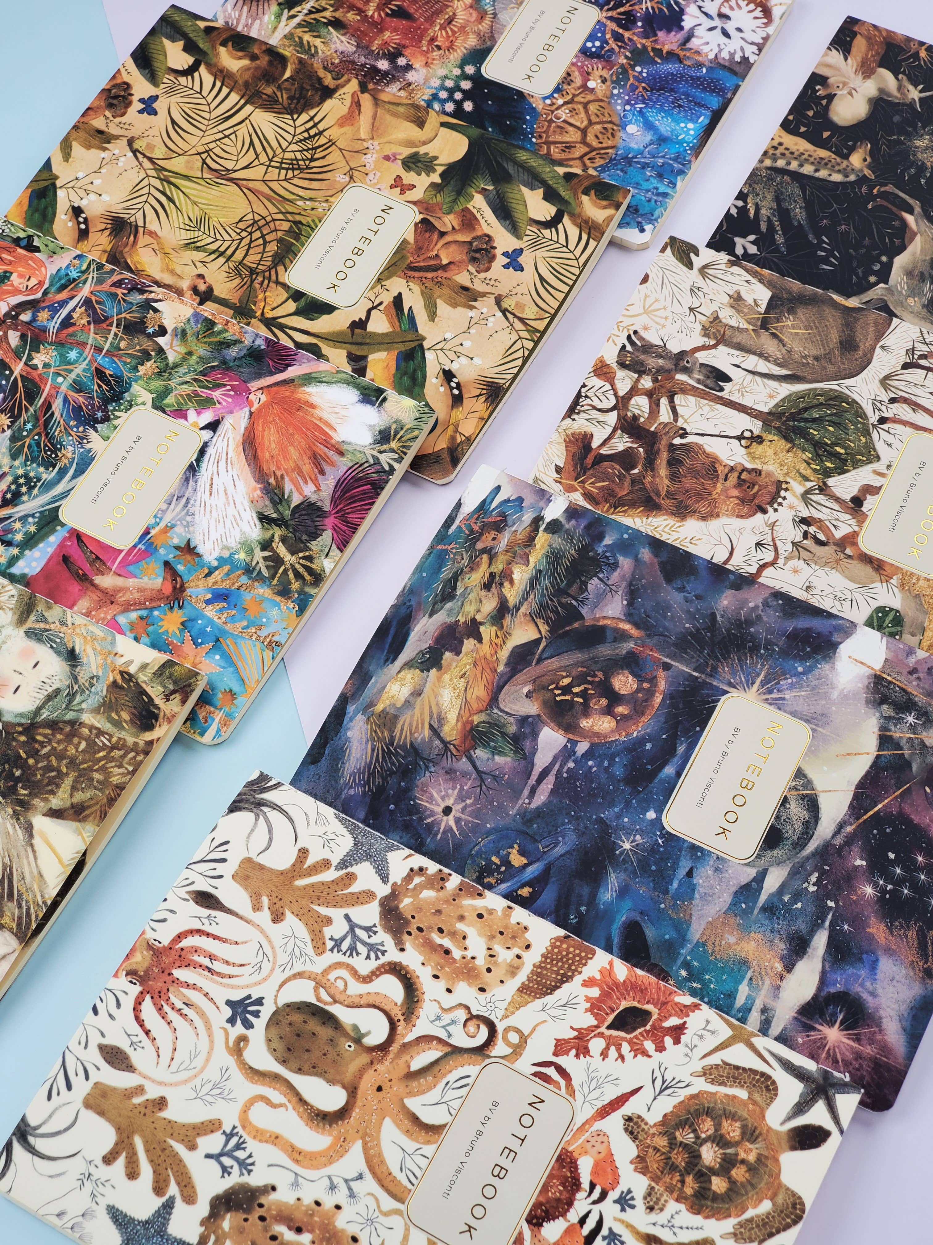 Collection of colorful notebooks with nature-themed designs on a light blue surface.