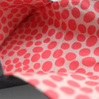 Close-up of a fabric surface with a repeating red polka dot pattern on a light pink background.