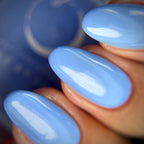 Close-up of fingernails painted with glossy light blue nail polish, with a blurred blue bottle in the background.