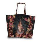 A large tote bag featuring a gothic floral print with a central illustration of a hand with rings and a pearl necklace, set against a dark textured background.