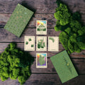 Set of tarot cards with green designs on a wooden surface surrounded by greenery