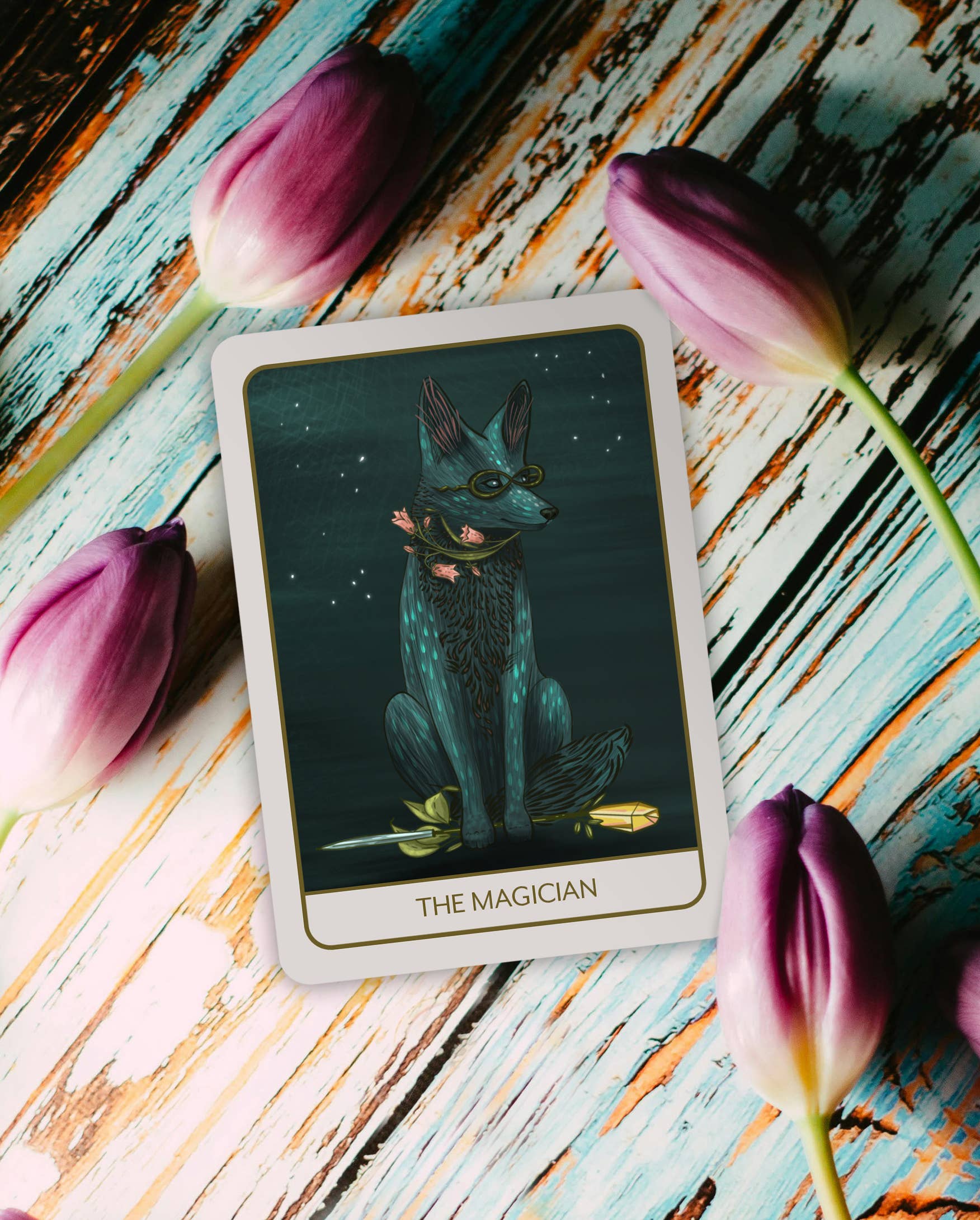 Tarot card titled 'The Magician' on a wooden surface with pink flowers.