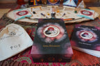 The Alchemical Self journal box set by Anna Boussquet, featuring the main box in the center, a matching book on the right, a white drawstring bag on the left, and other mystical props arranged on a table in the background.
