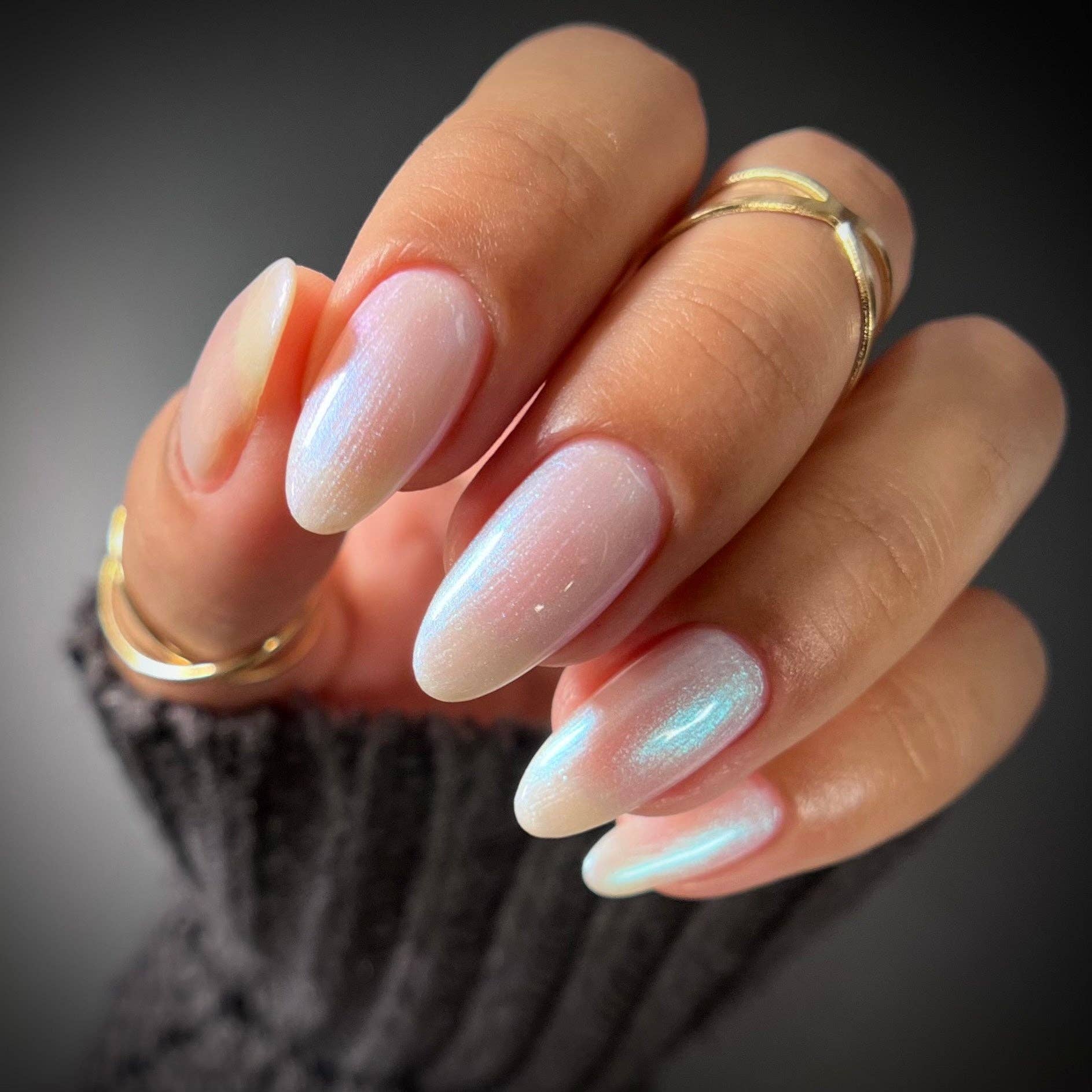 Close-up of a hand with soft pink nail polish and gold rings on a blurred background