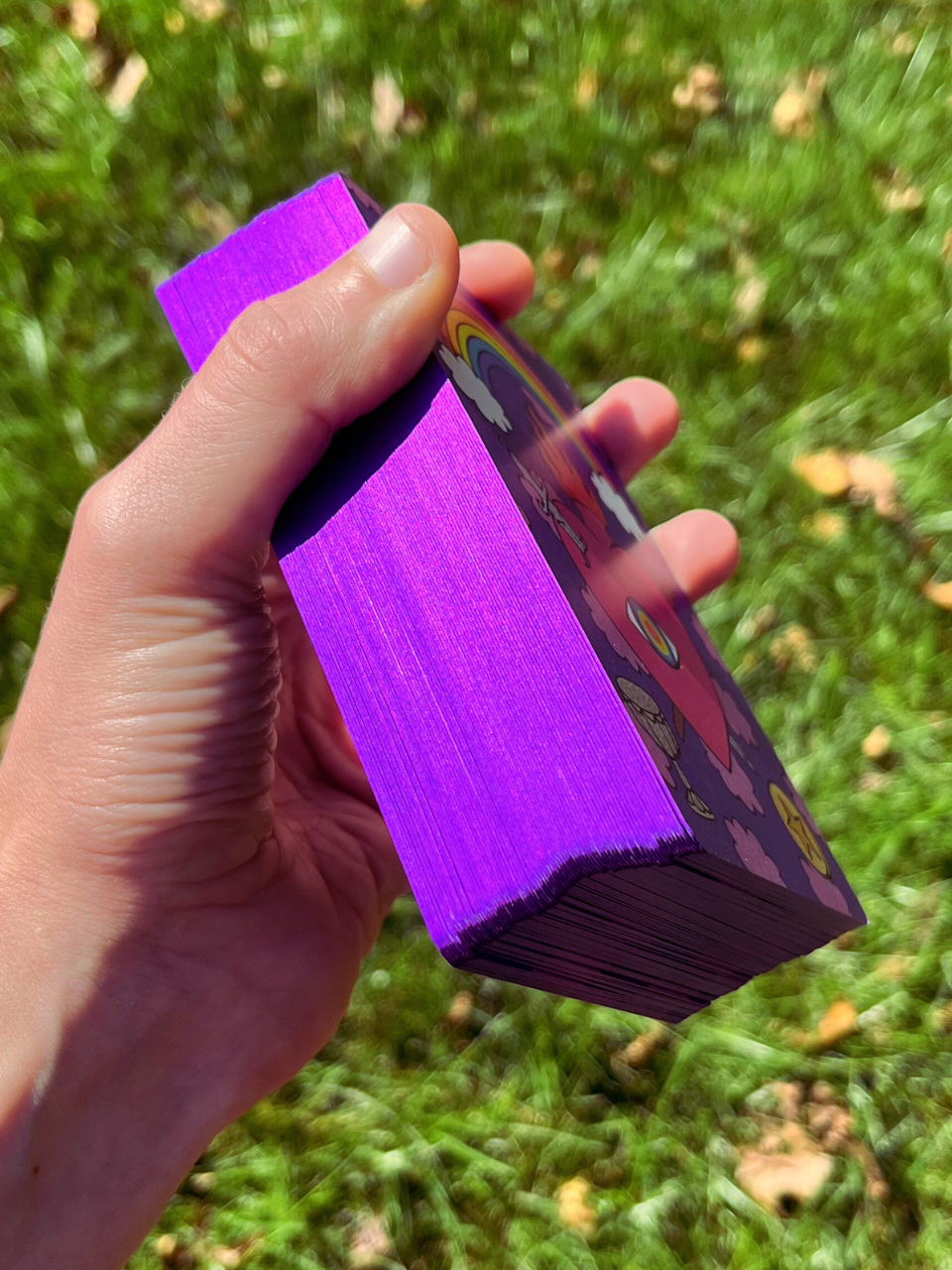 Hand holding a deck of purple cards against a grassy background