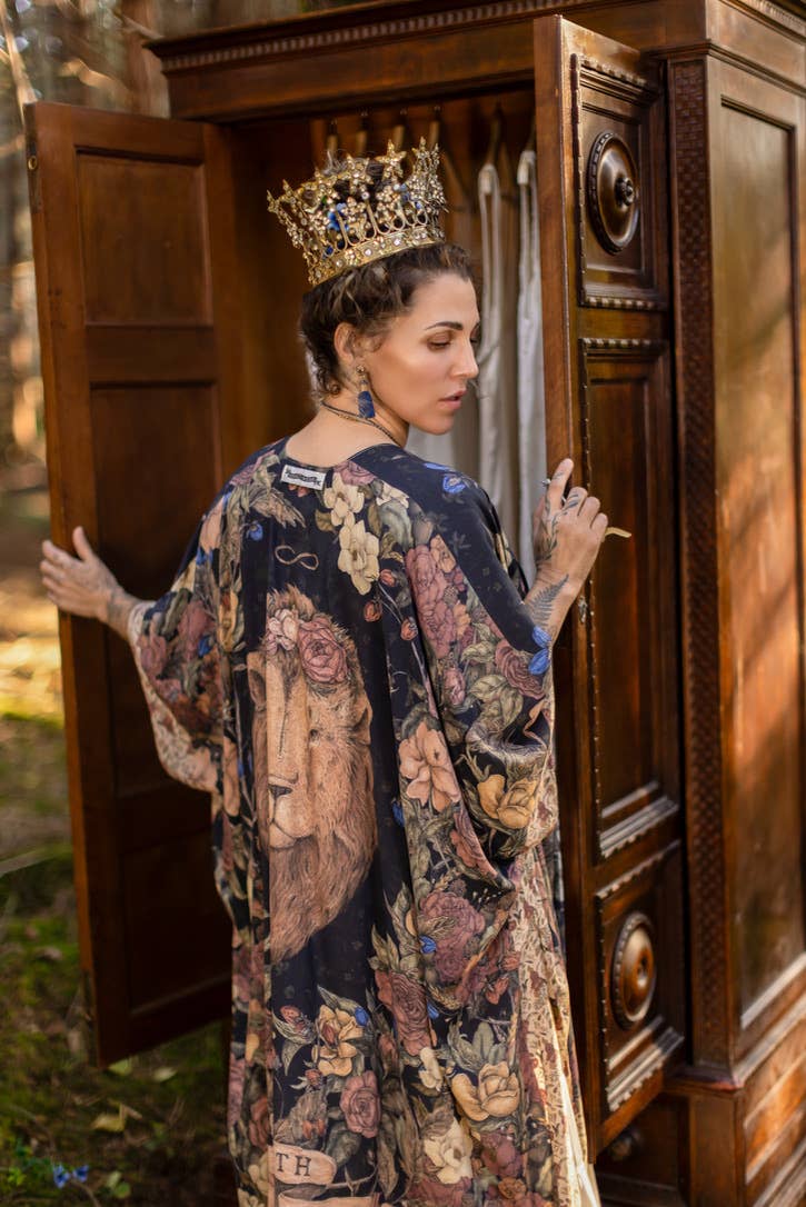 Woman in a floral dress and crown standing in front of an ornate wooden wardrobe.