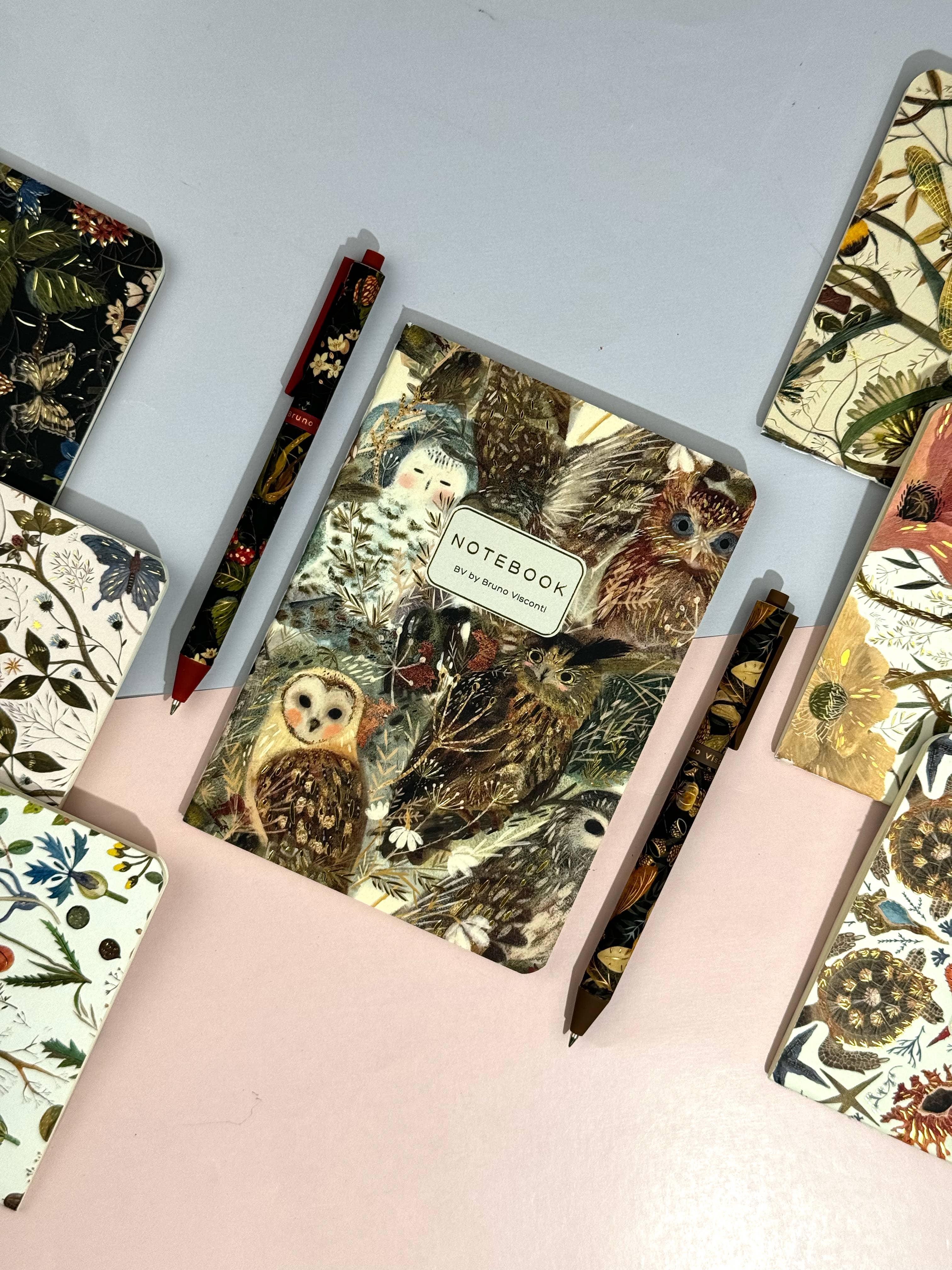 Hand holding a notebook with nature-themed cover against a light gray background