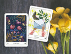 Two tarot cards with floral and butterfly designs on a dark surface with yellow flowers.
