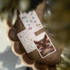 Three decorative playing cards are arranged on a scalloped brown tray. One card shows a close-up portrait of a brown cat with green eyes and small red hearts in the corners.