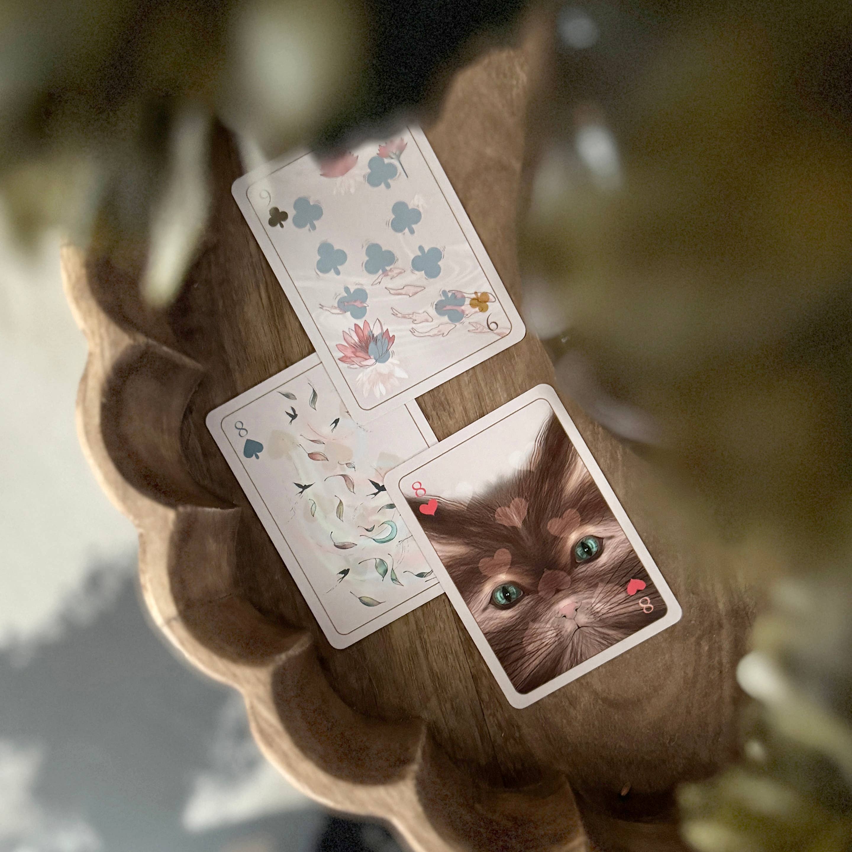 Three decorative playing cards are arranged on a scalloped brown tray. One card shows a close-up portrait of a brown cat with green eyes and small red hearts in the corners.