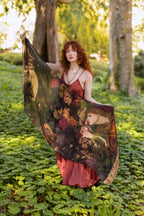 Woman holding a large, ornate fabric with floral patterns in a forest setting