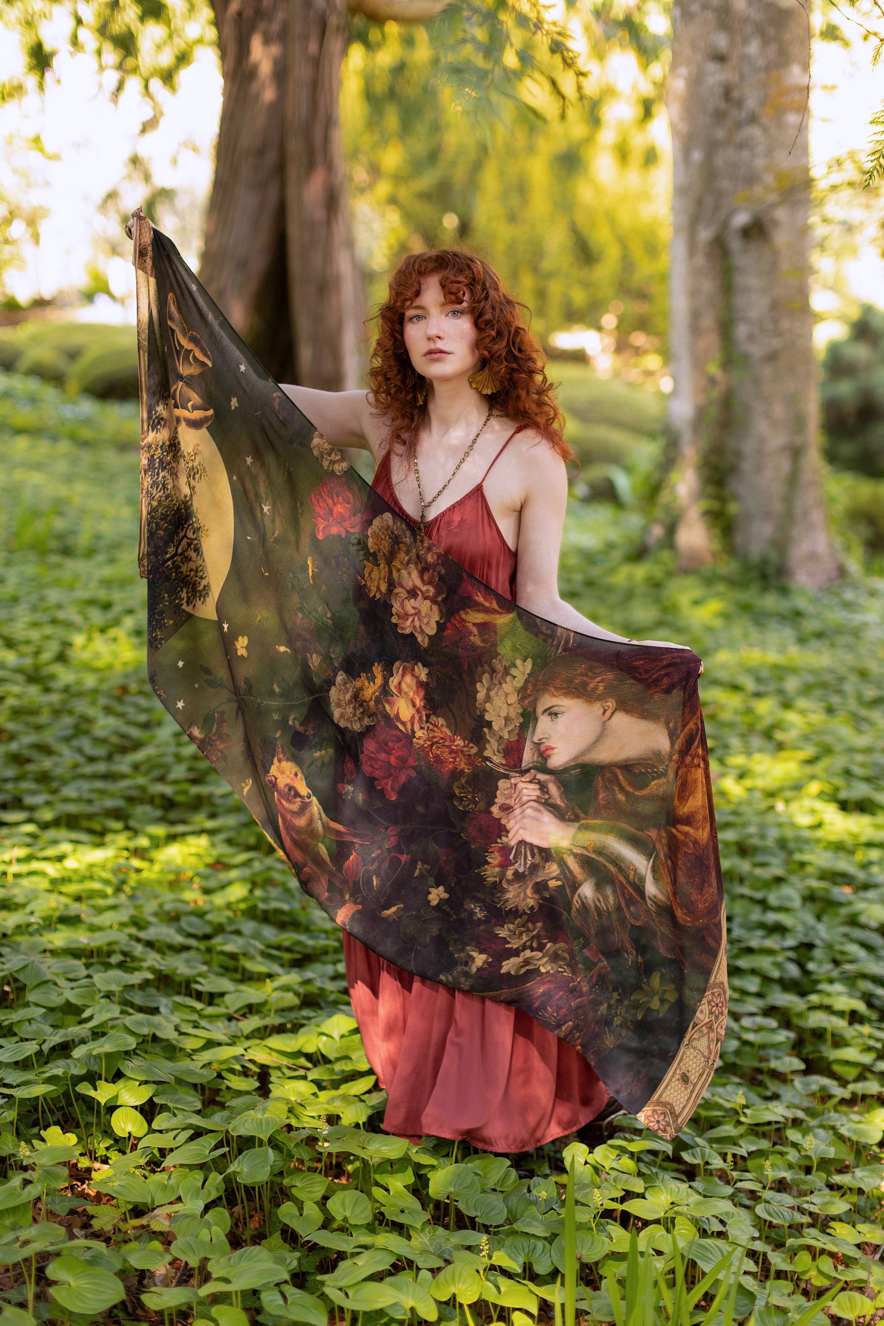 Woman holding a large, ornate fabric with floral patterns in a forest setting