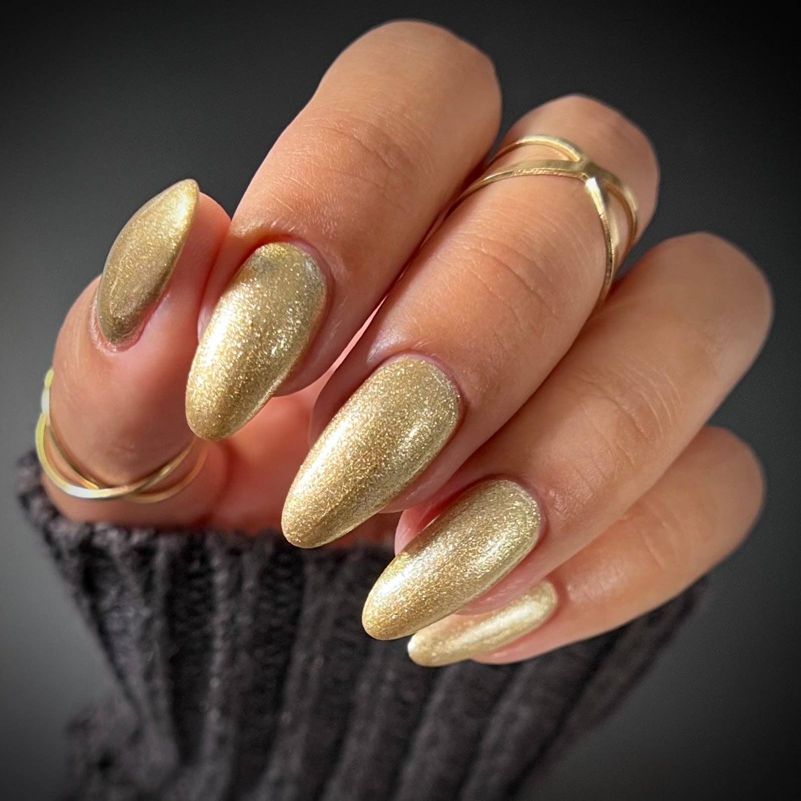 Hand with gold glittery nails and multiple rings on a dark background