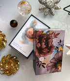 A boxed card or art product displayed on a light surface with decorative crystals and sequined props. The main sellable item appears to be the printed box set: one open card showing abstract artwork with the text 'SUNSTONE' and 'empirical truth, originally.
