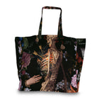 A large tote bag featuring a dark, gothic art print of a skeleton with flowers and a hand, on a white background.
