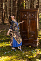 Woman in a floral dress standing next to a wooden cabinet in a forest setting