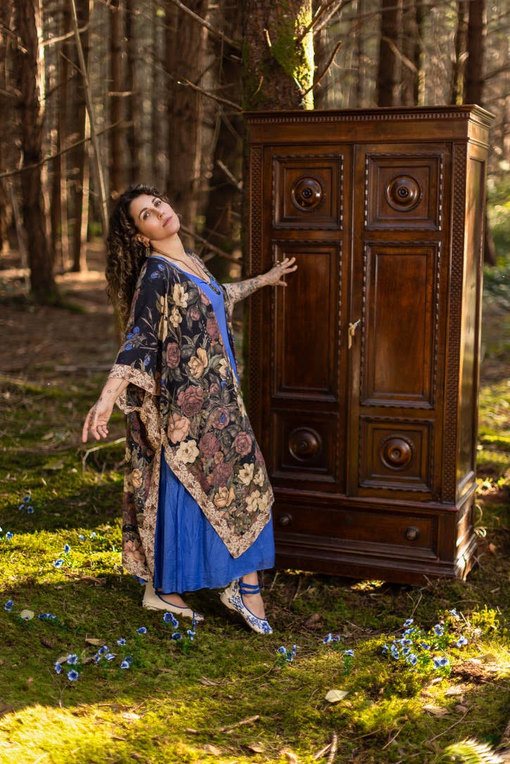 Woman in a floral dress standing next to a wooden cabinet in a forest setting