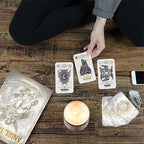 Person playing with tarot cards on a wooden surface with a candle and phone.
