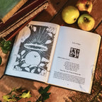 Open book with illustrations and text on a wooden surface with apples