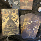 Grim Tales Tarot cards and companion book on a dark textured surface with decorative elements.