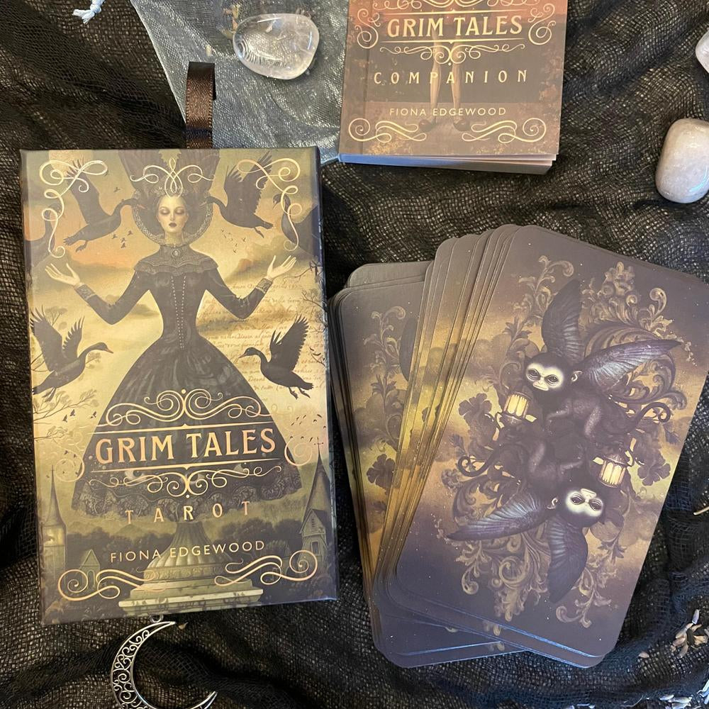 Grim Tales Tarot cards and companion book on a dark textured surface with decorative elements.