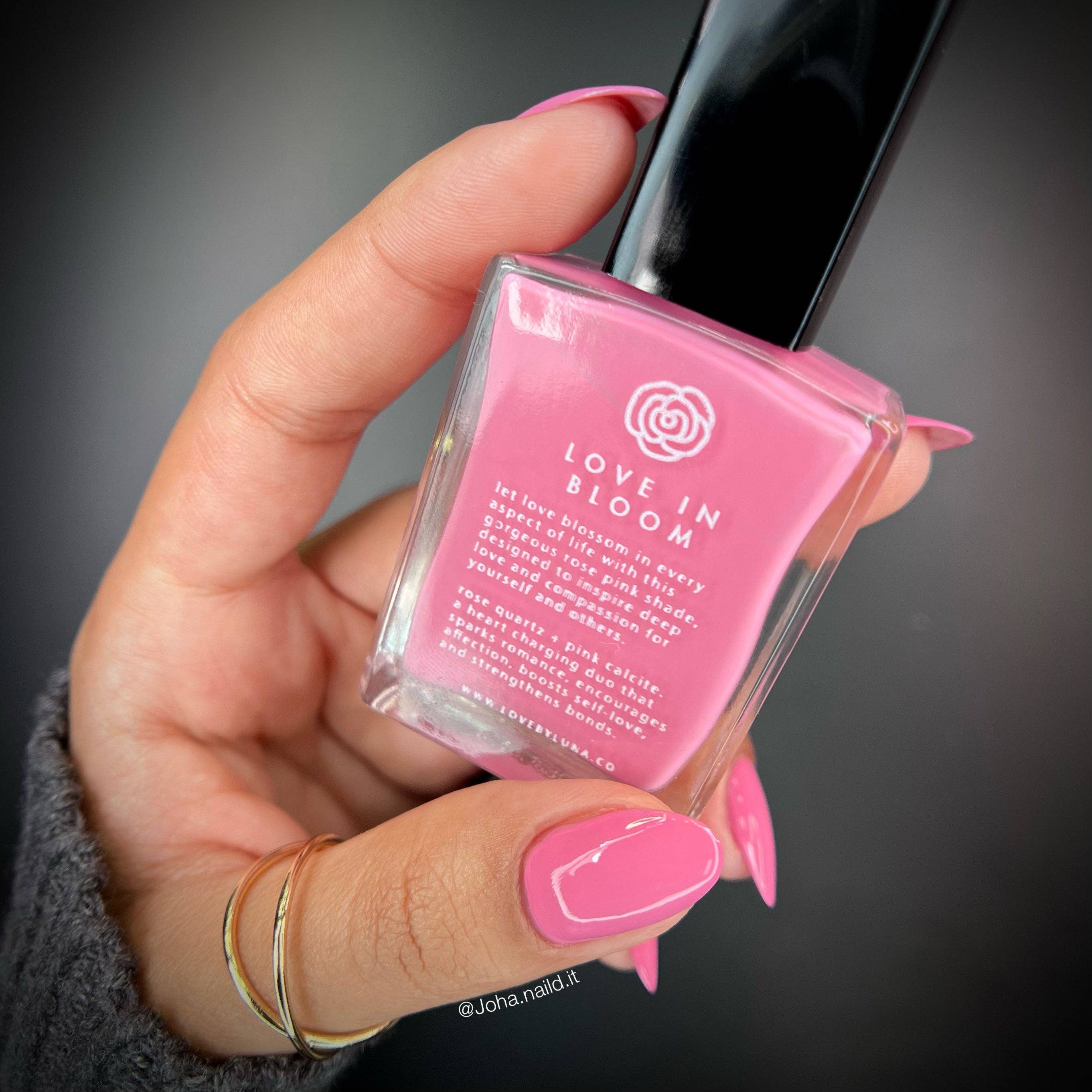 Hand holding a pink nail polish bottle with 'Love in Bloom' text on a dark background