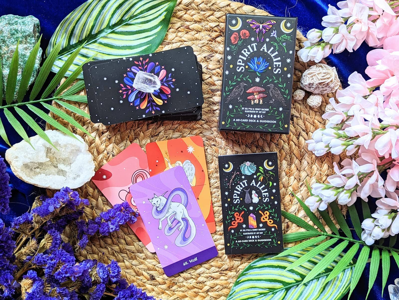 Collection of tarot cards with colorful designs on a woven mat surrounded by plants and flowers.