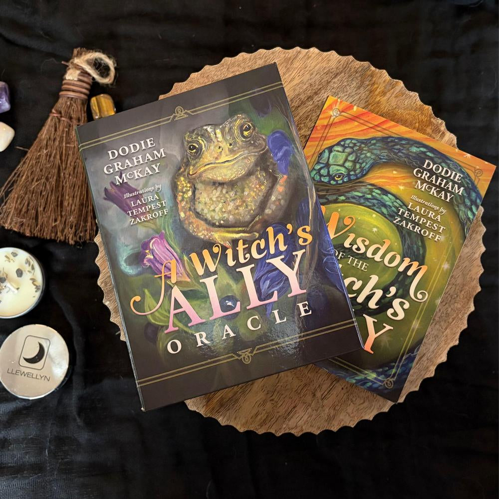 Two oracle cards from 'A Witch's Ally Oracle' on a dark surface with a broom and other items.